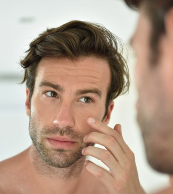 man applying face cream in front of mirror